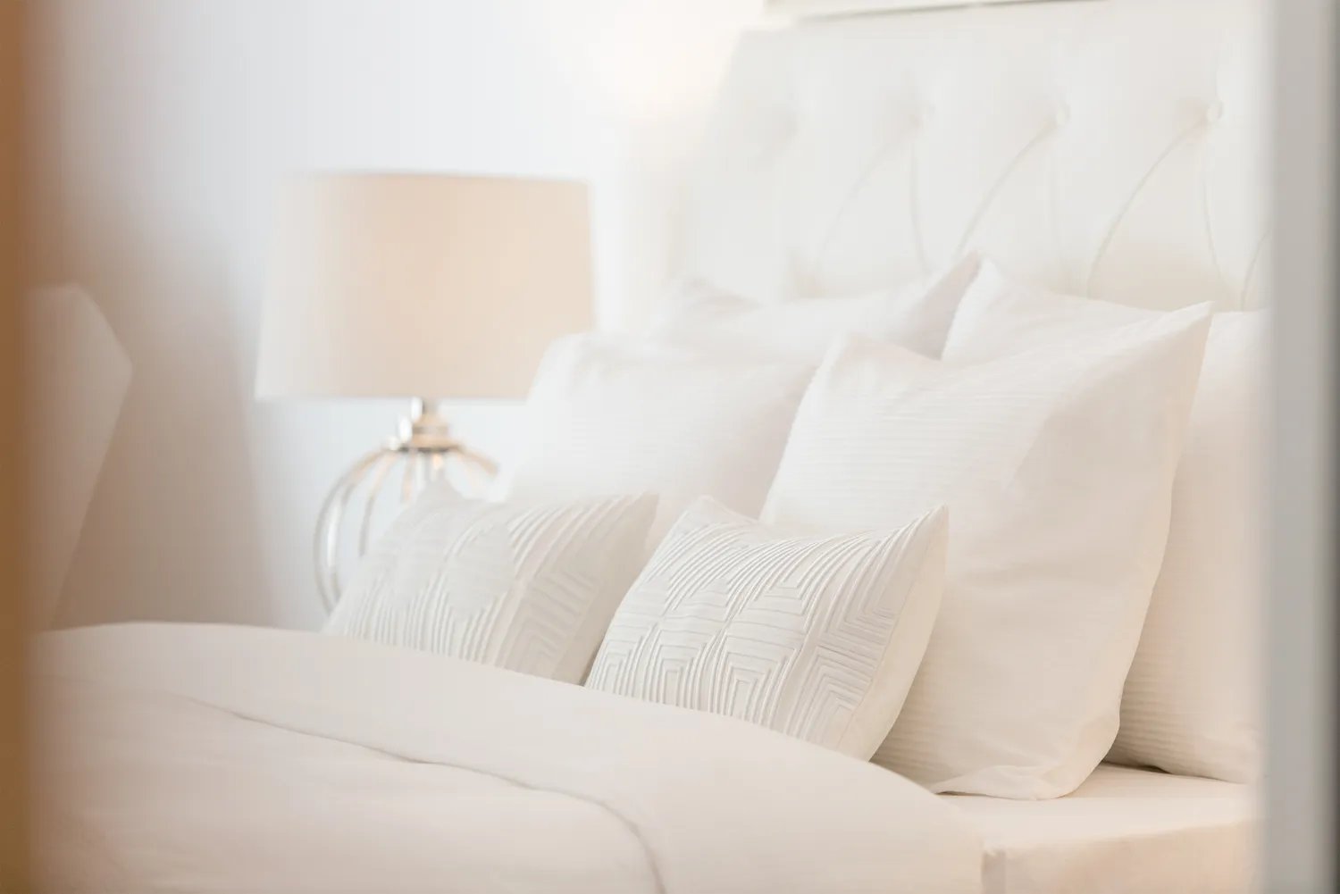 White upholstered bed with white bedding and metal lamp with white shade next to the bed