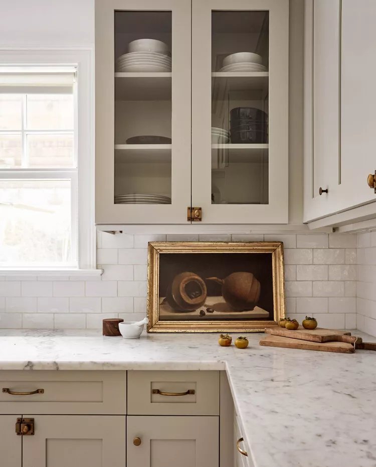 A kitchen with white walls, white backsplash tiles, white marble countertops, and off-white kitchen cabinets