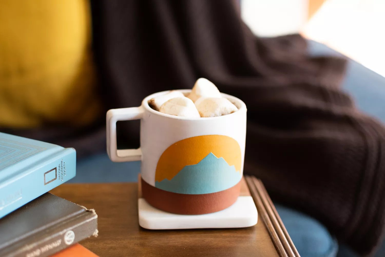 Marshmallows on top of hot beverage in painted mug with mountain-scape closeup