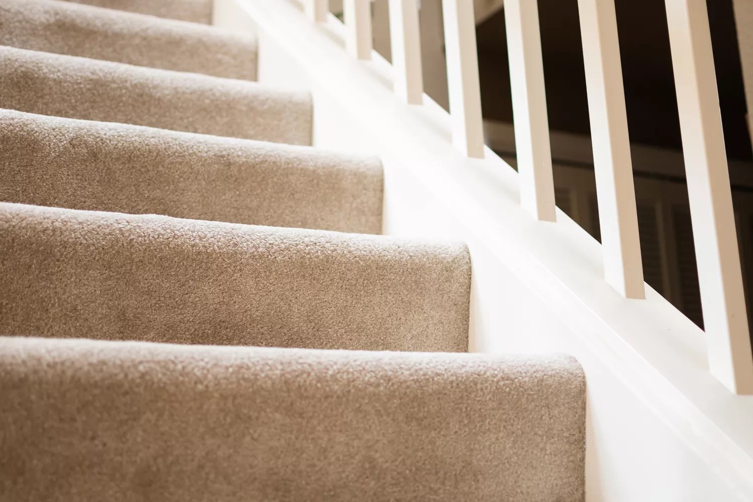 Tan carpeted stairs with white railing closeup