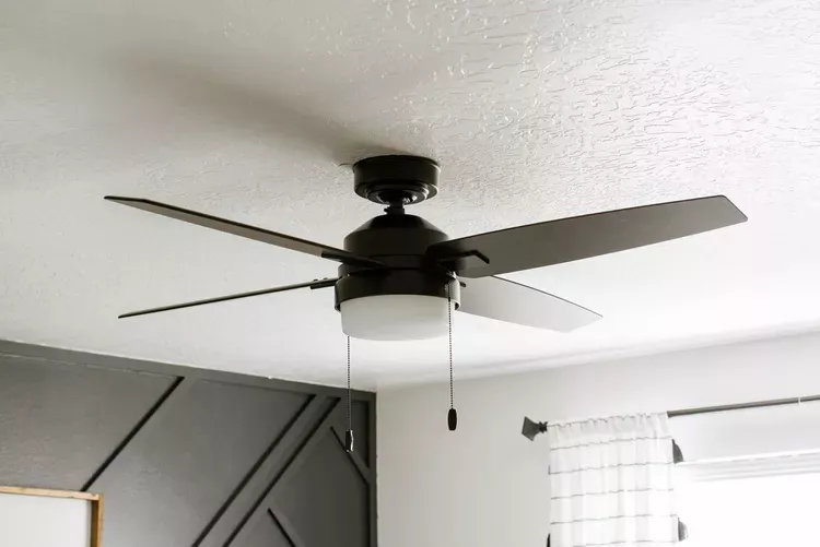 A black ceiling fan in a bedroom with a black accent wall in the background.